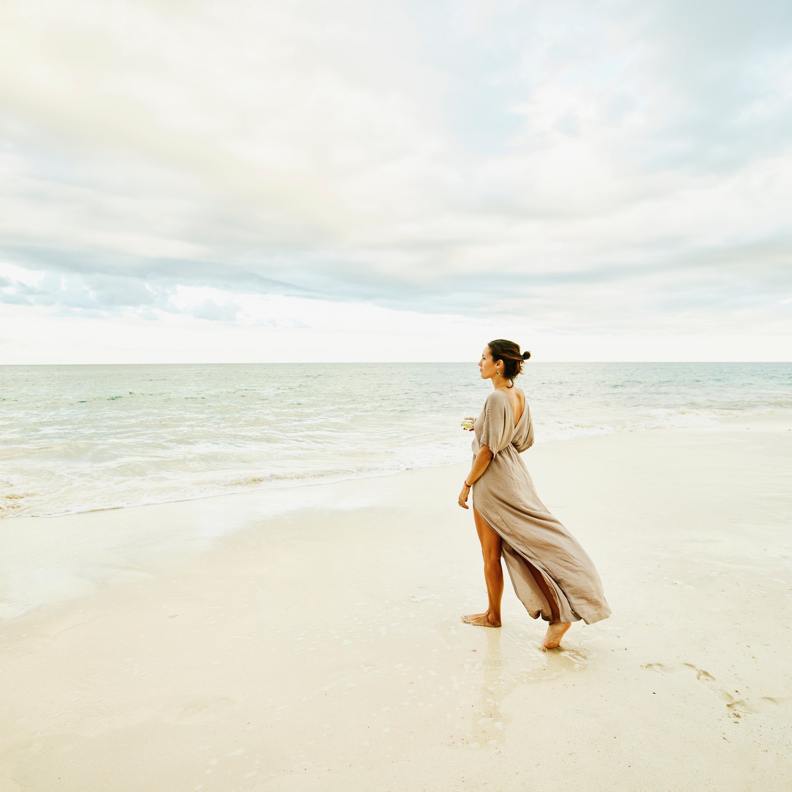 Wide shot of woman walking on beach and enjoying sunset at tropical resort
